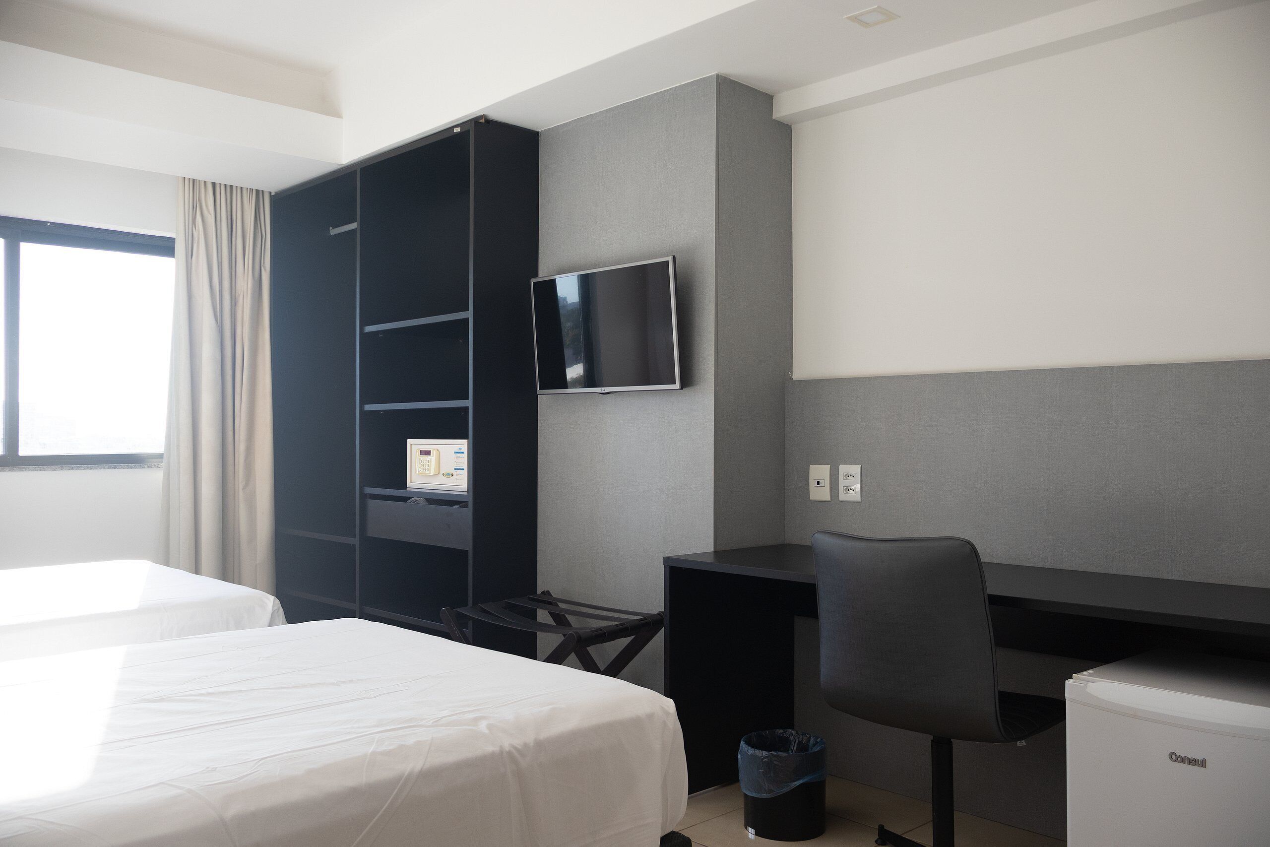 Una habitación de hotel con cama, escritorio, silla, televisor y armario.