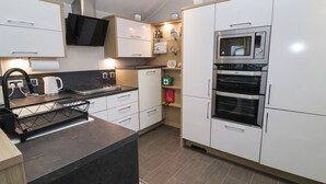 A modern kitchen with white cabinets, a black countertop, a built-in oven, and a microwave. - Osprey Court 1 (Great Yarmouth)
