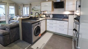 A compact kitchen with a washing machine, a dining area with a table and chairs, and a sofa. - Osprey Court 1 (Great Yarmouth)