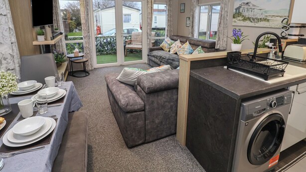 A compact living space with a sofa, dining table, and a washing machine. - Osprey Court 1 (Great Yarmouth)