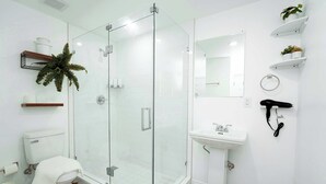 A modern bathroom with a glass-enclosed shower, a toilet, a sink, and a mirror. - Modern Boho Studio Near Miami River (Miami)