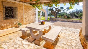 Un patio de piedra al aire libre con una mesa y bancos, rodeado por un muro de piedra y una pérgola cubierta de hiedra.