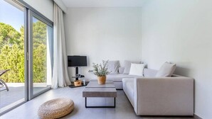 Ein modernes Wohnzimmer mit einer Couch, einem Couchtisch, einem Fernseher und einem großen Fenster mit Vorhängen.
