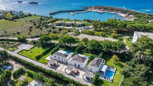 Vue aérienne d’une propriété située sur la côte, comprenant un port de plaisance, plusieurs maisons et une grande piscine.