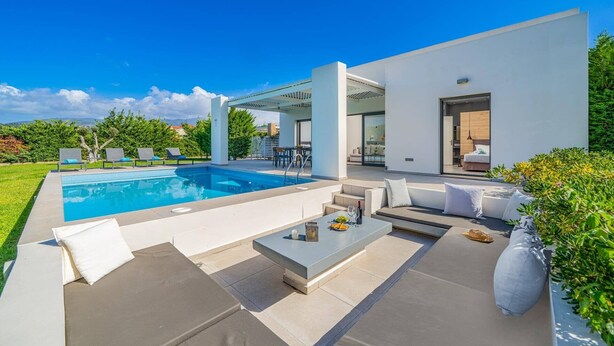 Un espace piscine extérieur moderne, doté d’une piscine à l’eau d’un bleu limpide, de chaises longues blanches et d’un coin repas avec une table et des chaises.
