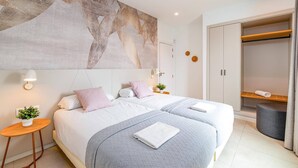 Een moderne slaapkamer met twee bedden, een groot abstract schilderij, een inloopkast en een klein bijzettafeltje met een plant.