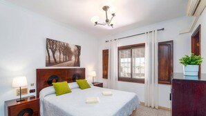 Une chambre à coucher avec un lit, une table de chevet, une lampe, un tableau, une fenêtre et une plante.