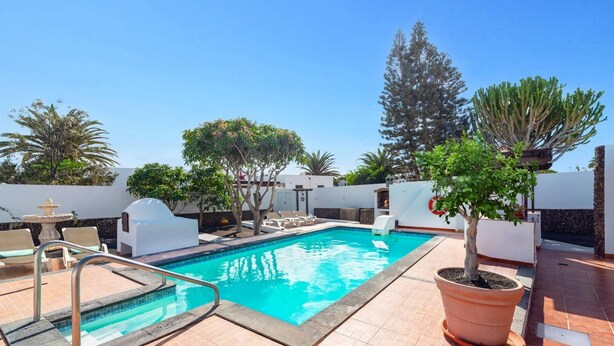 Une piscine avec une terrasse carrelée, des chaises longues et des plantes en pot.