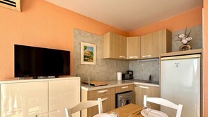 Una cocina compacta con televisor, refrigerador y mesa de comedor lista para cuatro personas.