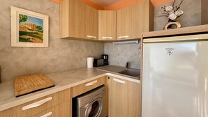 Una cocina compacta con armarios de madera, lavadora, refrigerador y cafetera.