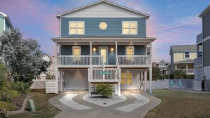 A two-story house with a balcony, a front porch, and a small garden area. - "The Palm House": A pool, hot tub & ICWW views! (Carolina Beach)