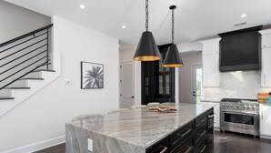 A modern kitchen with a marble island, black cabinets, stainless steel appliances, and pendant lighting. - "The Palm House": A pool, hot tub & ICWW views! (Carolina Beach)