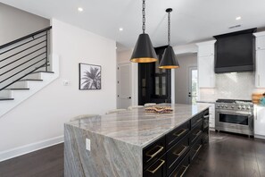 A modern kitchen with a marble island, black cabinets, stainless steel appliances, and pendant lighting. - "The Palm House": A pool, hot tub & ICWW views! (Carolina Beach)