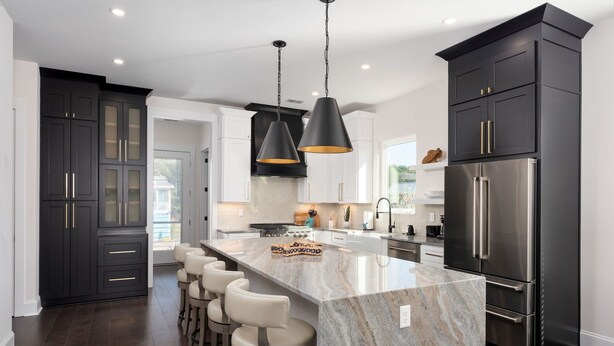 A modern kitchen with dark cabinetry, a central island with bar stools, stainless steel appliances, and pendant lighting. - "The Palm House": A pool, hot tub & ICWW views! (Carolina Beach)