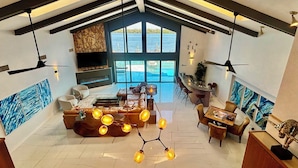 Een ruime woonkamer met een groot raam dat uitkijkt op een waterpartij, een open haard en een moderne zithoek.