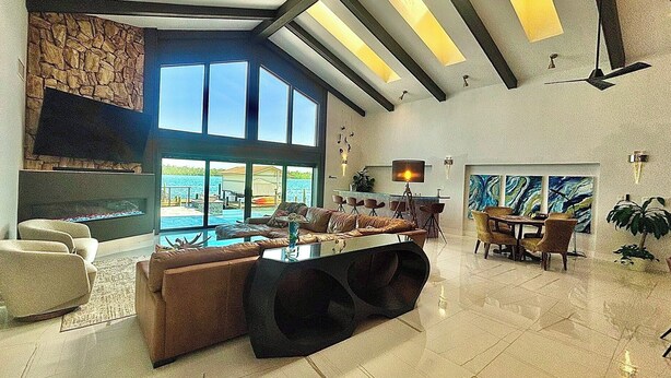 Een ruime woonkamer met een groot raam met uitzicht op een zwembad, een open haard en een eetgedeelte met uitzicht op de zee.