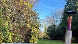 Un bain à remous en bois, doté d’une cheminée en métal, entouré d’une zone herbeuse et d’arbres.