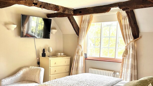 Une chambre à coucher avec un lit, des tables de chevet, une télévision et une fenêtre avec des rideaux.