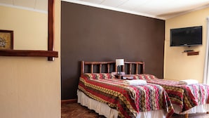 Ett hotellrum med två sängar, en sänggavel i trä, en tv som är monterad på väggen och ett trägolv med fiskbensmönster.