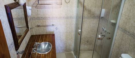 Un baño con tocador de madera, lavabo, cabina de ducha con mampara de vidrio e inodoro.