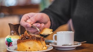En desserttallrik med en bit tårta och vispad grädde, en kopp kaffe och en dekorativ prydnad på ett bord.