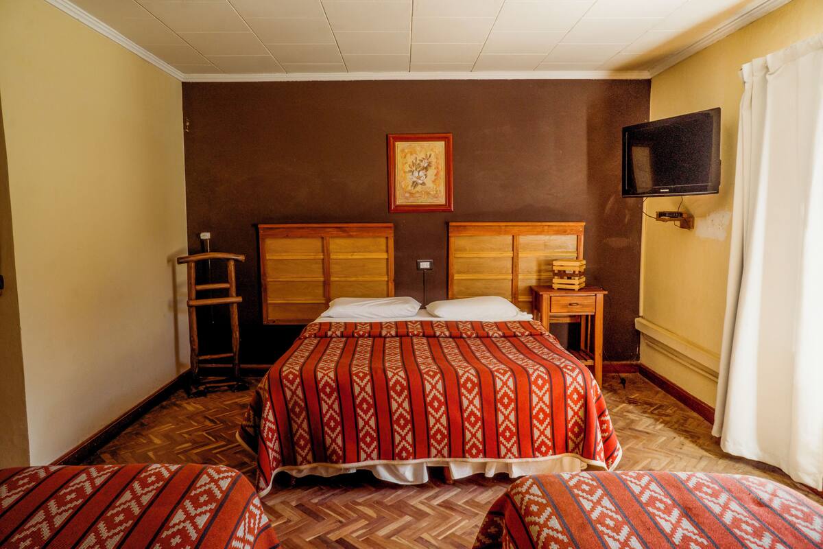 A hotel room with a large bed, two bedside tables, a TV mounted on the wall, and a wooden ladder.