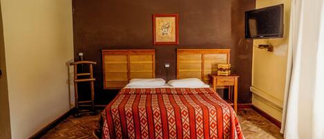 A hotel room with a large bed, two bedside tables, a TV mounted on the wall, and a wooden ladder.