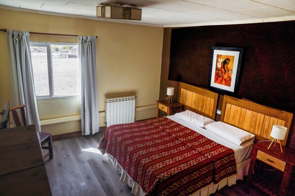 Une chambre d’hôtel avec un lit en bois, un bureau, une chaise, un radiateur et une fenêtre avec des rideaux.
