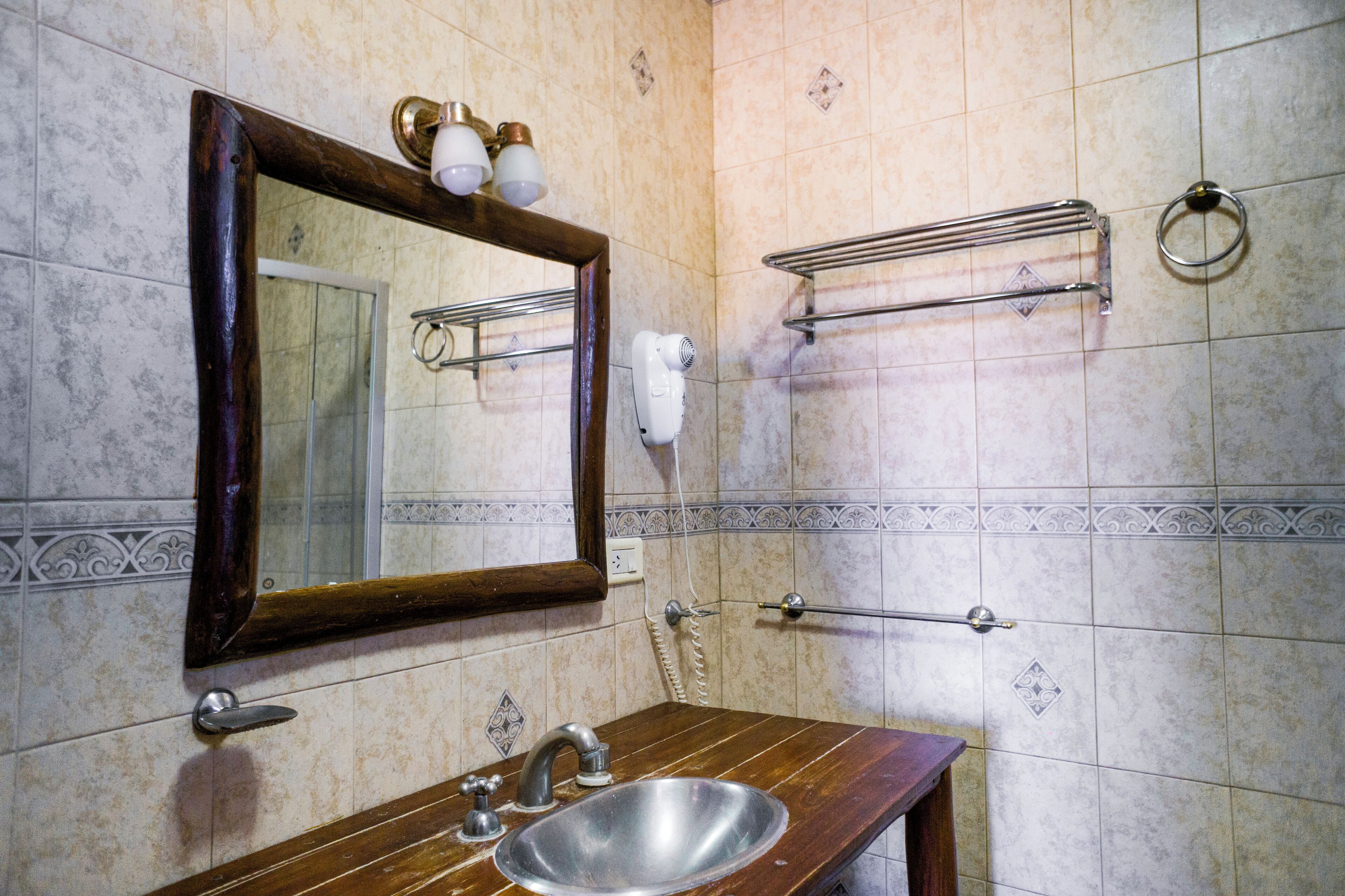 Un baño con tocador de madera, lavamanos, espejo, toallero y secador de pelo.