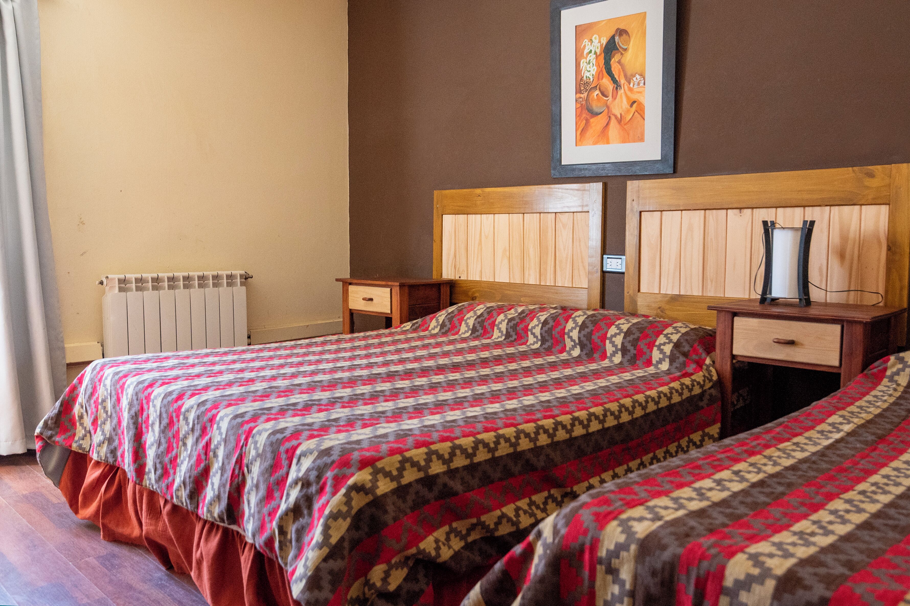 A bedroom with two beds, wooden headboards, a bedside table with a lamp, and a radiator.