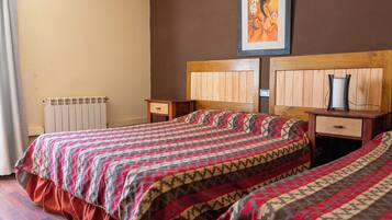 A bedroom with two beds, wooden headboards, a bedside table with a lamp, and a radiator.