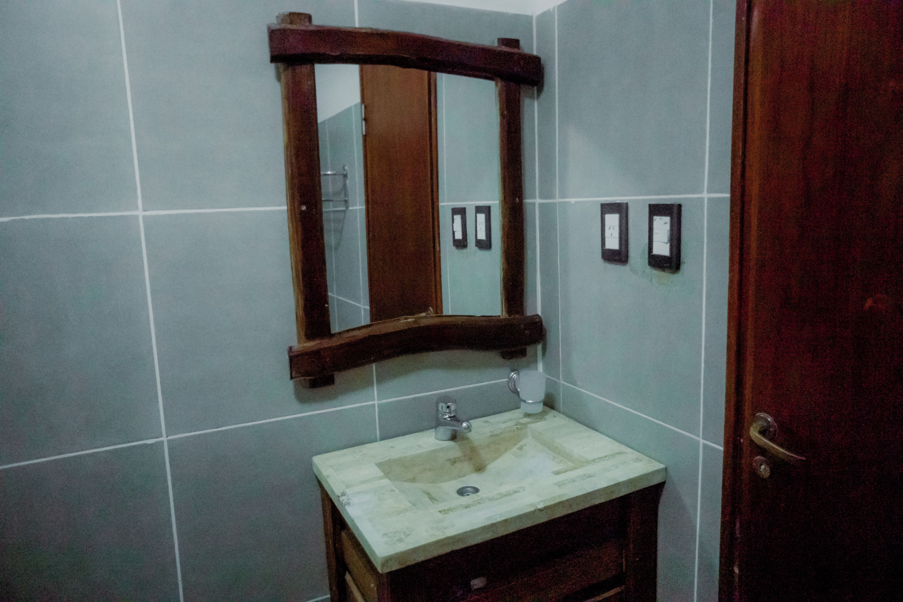 A bathroom with a wooden-framed mirror, a sink with a marble countertop, and a door.