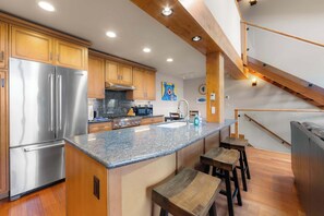 A modern kitchen with wooden cabinets, stainless steel appliances, granite countertops, and a built-in island with bar stools. - Aspen Edge, Lakefront and Loft (South Lake Tahoe)