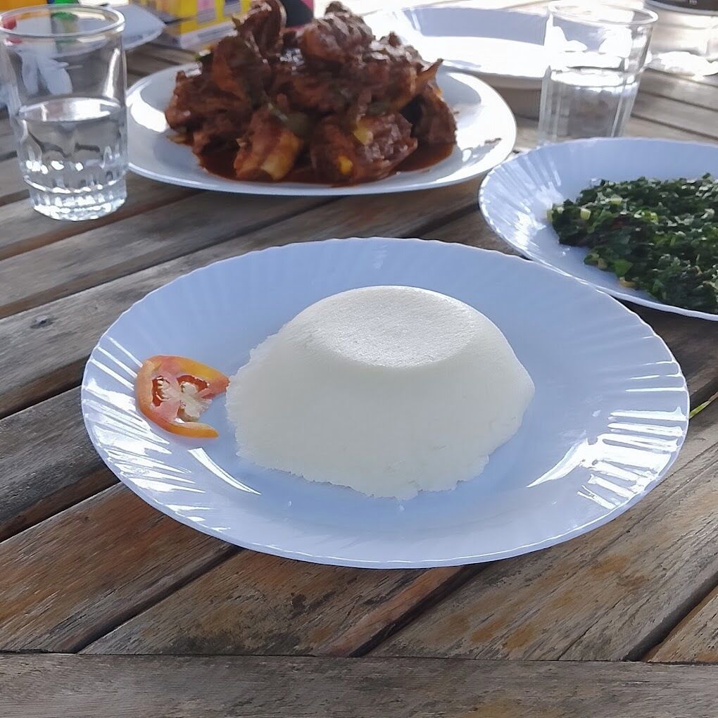 A white plate with a mound of rice and a small piece of tomato on a wooden table.