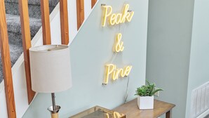 Una escalera con barandillas de madera, una lámpara, un letrero de neón que dice "Peak & Pine", una pequeña planta en maceta y una consola de madera con un tocadiscos.