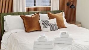 Una cama bien hecha con sábanas blancas, almohadas marrones y blancas, y dos toallas dobladas sobre la cama.