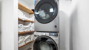 Eine gestapelte Waschmaschine und ein Trockner mit Regalen darüber, auf denen gefaltete Kleidung liegt.