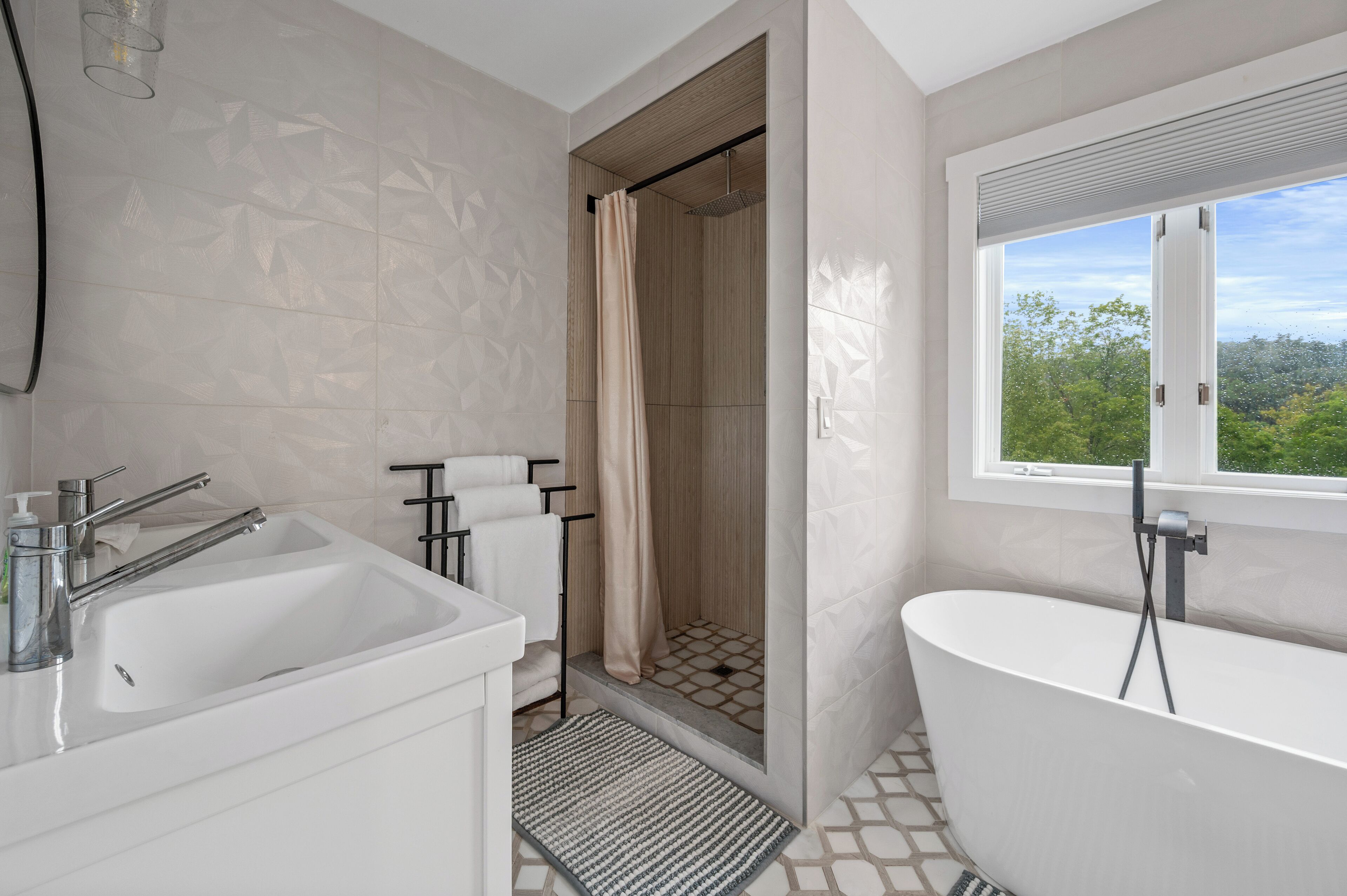 Ein modernes Badezimmer mit freistehender Badewanne, einer Duschkabine und einem großen Fenster mit Blick auf Grünflächen.