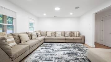 A modern living room with a beige sectional sofa, a patterned rug, and a white ceiling with recessed lighting.