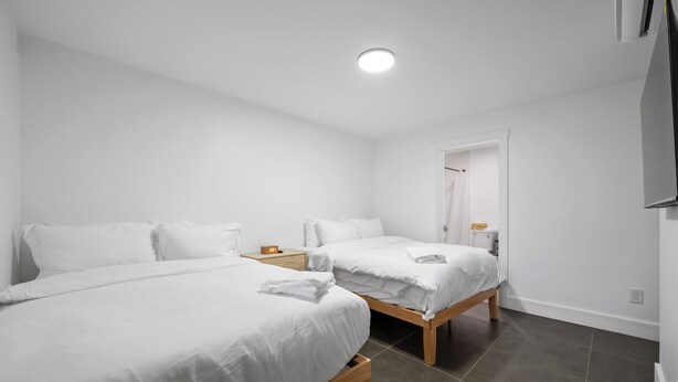 Ein modernes Hotelzimmer mit zwei Einzelbetten, einem Holfnachtschränkchen, einem kleinen Tisch und einem weißen Kleiderschrank.