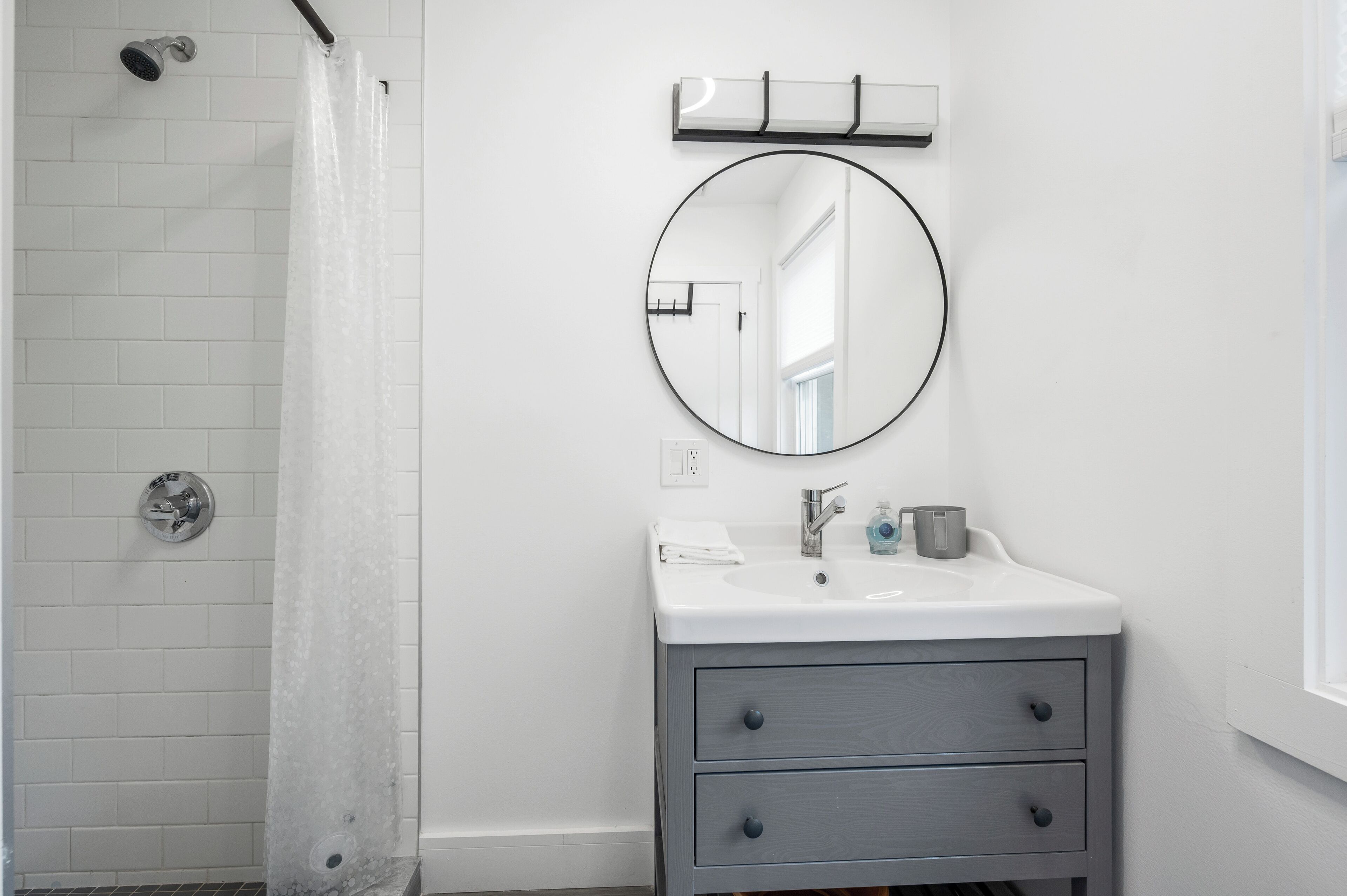 A bathroom with a shower, a sink with a mirror, and a window.