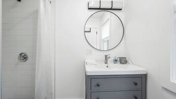 A bathroom with a shower, a sink with a mirror, and a window.