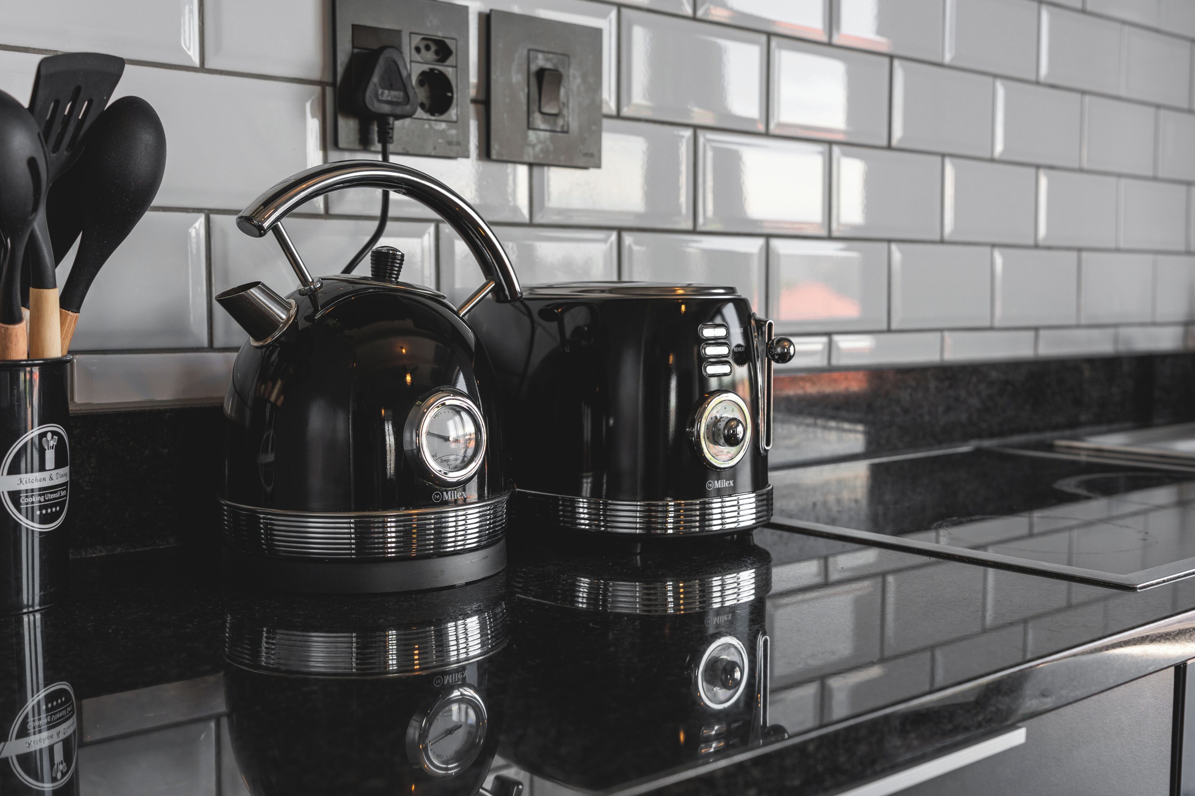 Una cocina con un hervidor negro y una cafetera sobre una encimera reflectante.
