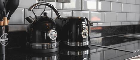 Una cocina con un hervidor negro y una cafetera sobre una encimera reflectante.