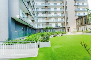 A modern multi-story building with balconies, a courtyard with artificial grass, and planters. - Modern Executive Studio Apartment at Lennox (Accra)