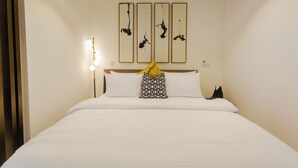 A neatly made bed with white linens and a patterned pillow, a bedside lamp, and a wall-mounted light fixture. - Modern Executive Studio Apartment at Lennox (Accra)