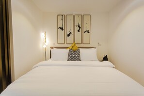 A neatly made bed with white linens and a patterned pillow, a bedside lamp, and a wall-mounted light fixture. - Modern Executive Studio Apartment at Lennox (Accra)