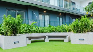 A modern building with a balcony, large windows, and a well-maintained garden area with planters and benches. - Modern Executive Studio Apartment at Lennox (Accra)