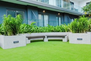 A modern building with a balcony, large windows, and a well-maintained garden area with planters and benches. - Modern Executive Studio Apartment at Lennox (Accra)