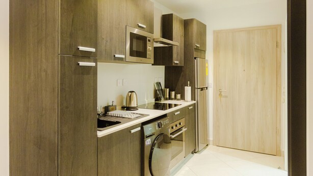 A modern kitchen with wooden cabinets, stainless steel appliances, and a tiled floor. - Modern Executive Studio Apartment at Lennox (Accra)